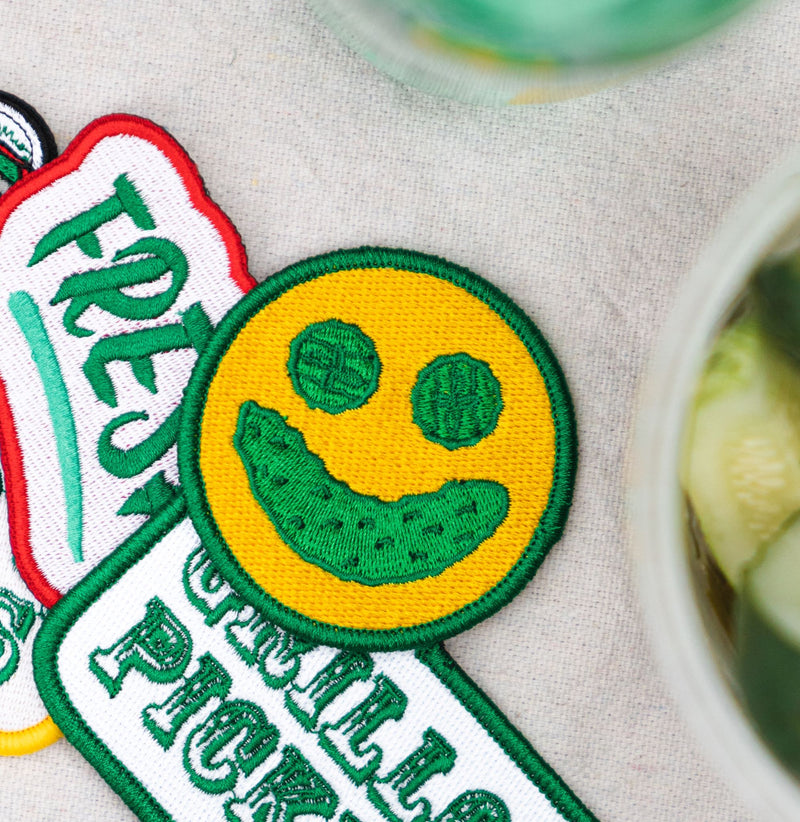 smiley face with pickle smile embroidered patch next to other grillo's pickles patches